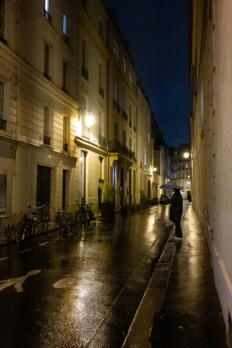 Ambiance nocturne dans une rue de Paris éclairée par des lampadaires tungstène, avec balance des blancs corrigée