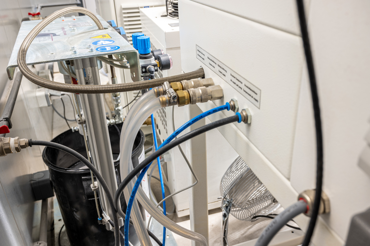 Photo horizontale, gros plan technique, environnement de laboratoire industriel, absence de personnes, tuyaux et raccords visibles, ambiance propre et professionnelle, profondeur de champ modérée, couleurs dominantes blanc, métal, bleu et noir, sujet lié à la pneumatique, à l’automatisation et aux procédés industriels.